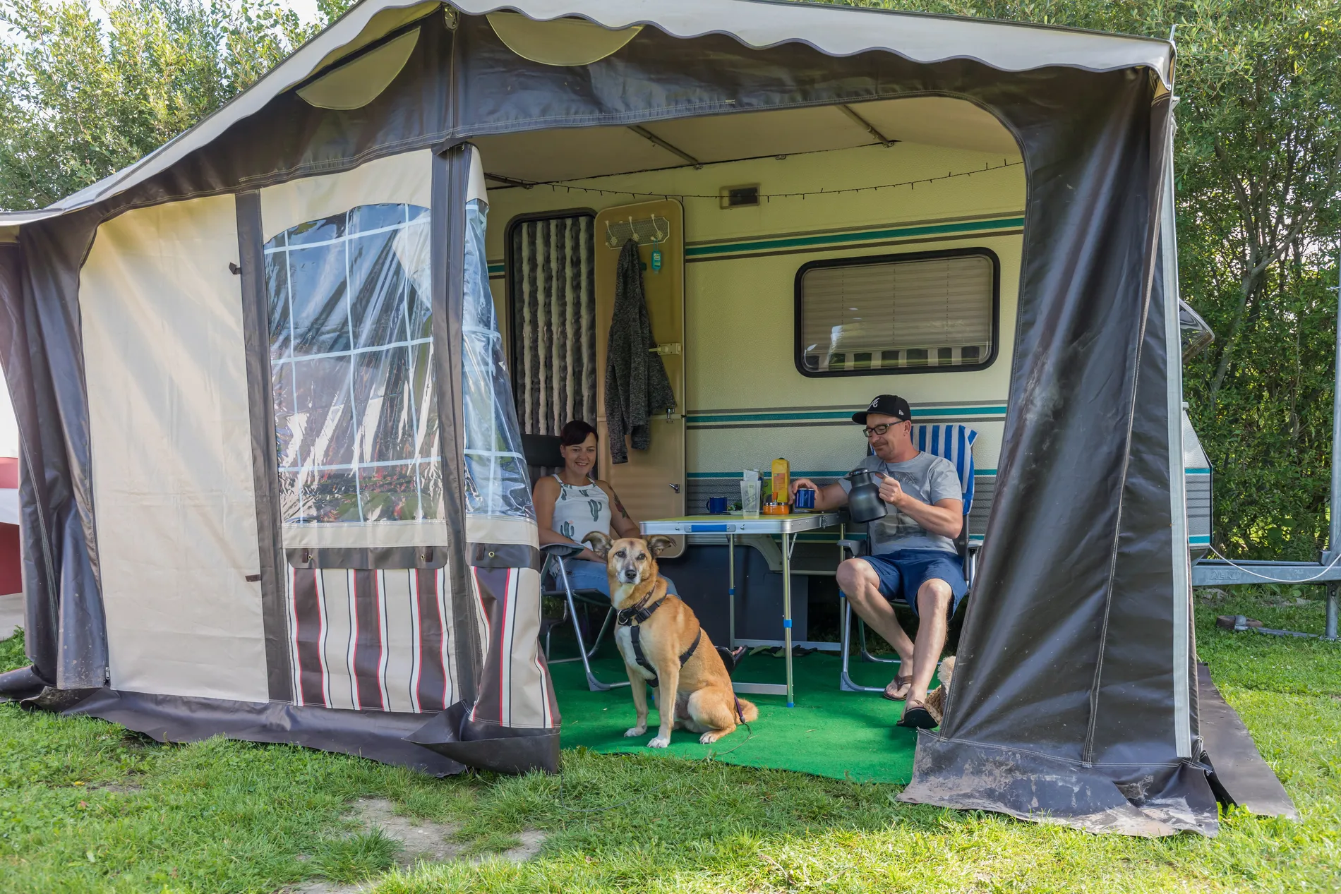 Gasten genieten van hun vakantie met de hond voor een caravan met voortent op een groene kampeerplaats bij Resort Land & Zee.